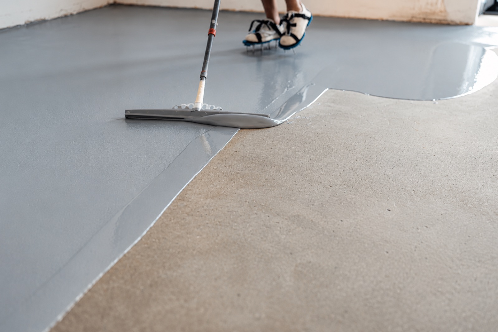 Gray epoxy coating being squeegeed onto a concrete floor during installation